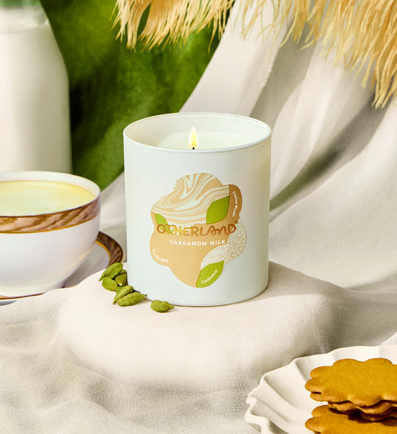 Candle with a Otherland logo on a table with cookies and greenery