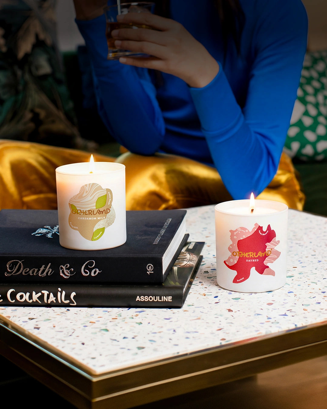 Two candles on a table with a book titled 'Death & Co' and a glass in the background.