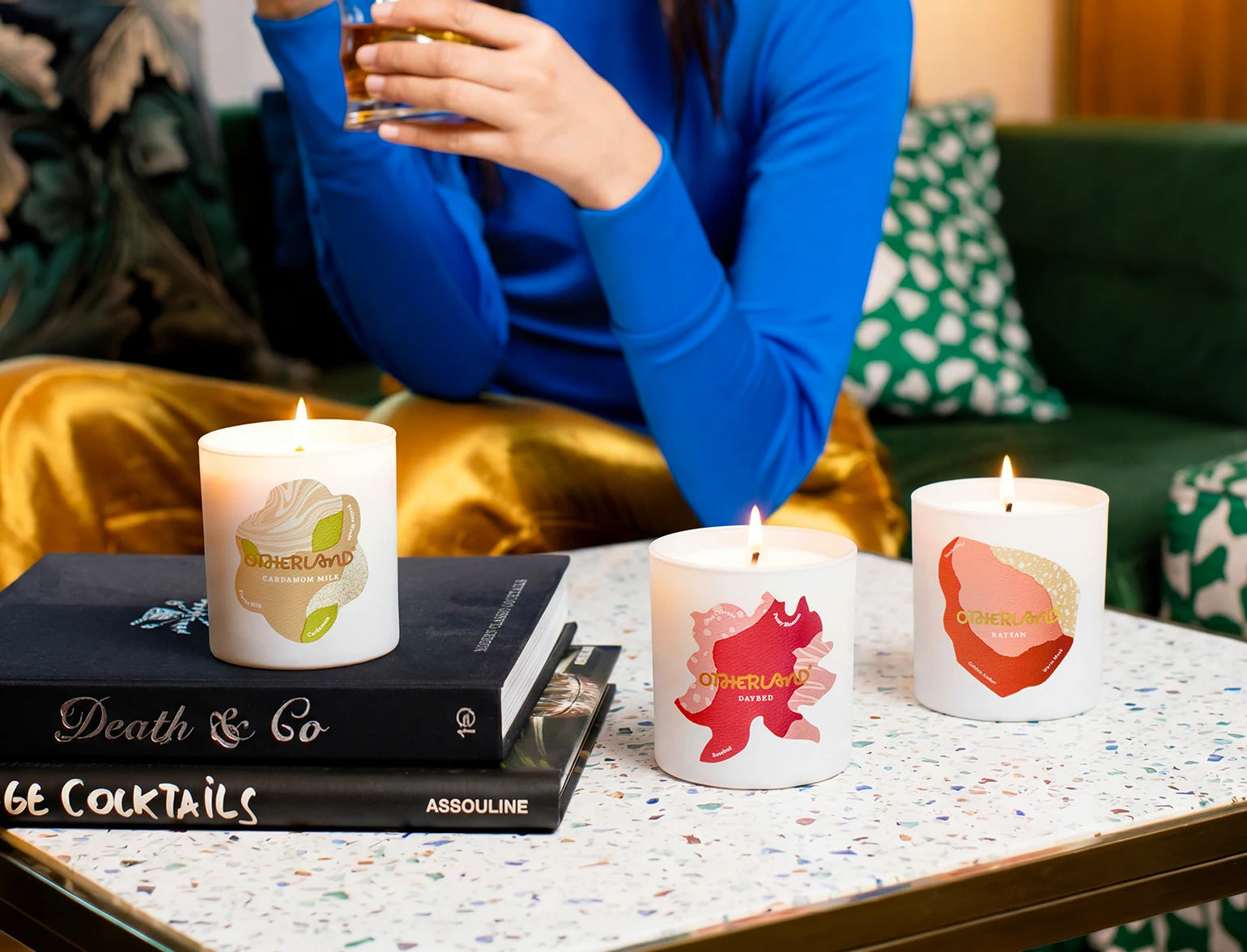 Candles with artistic designs on a table with a person holding a drink in the background.