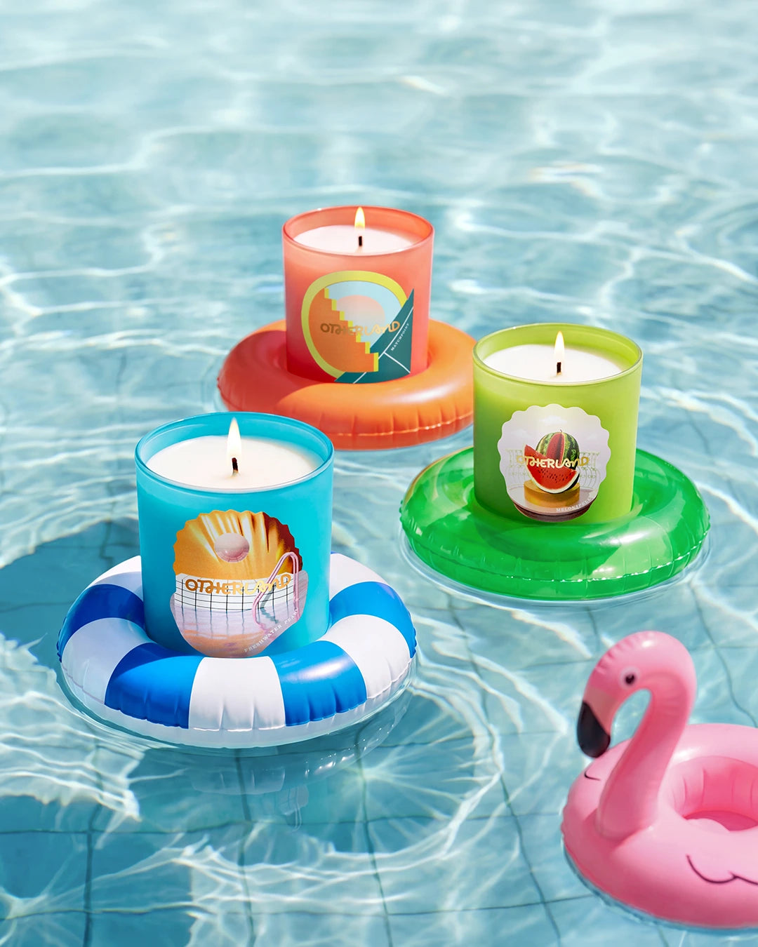 Four colorful candles on inflatable rings floating in water with a pink flamingo floatie.