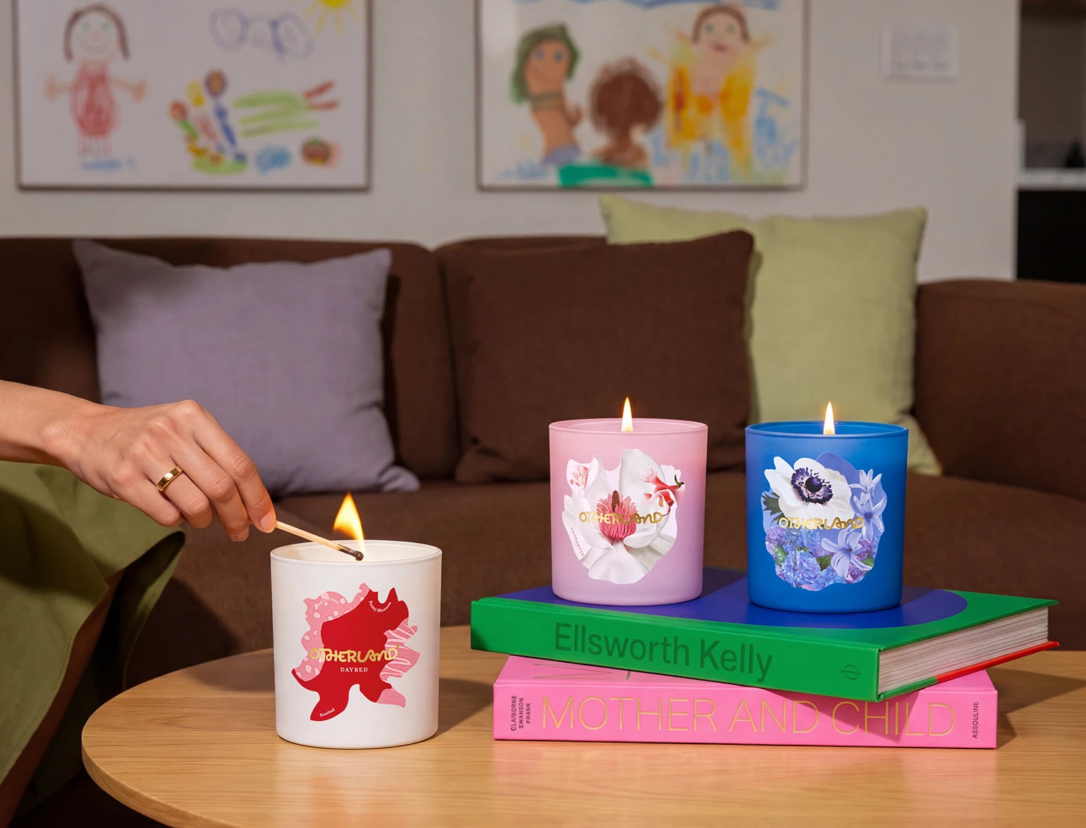 Person lighting a candle on a table with decorated candles and books in the background.