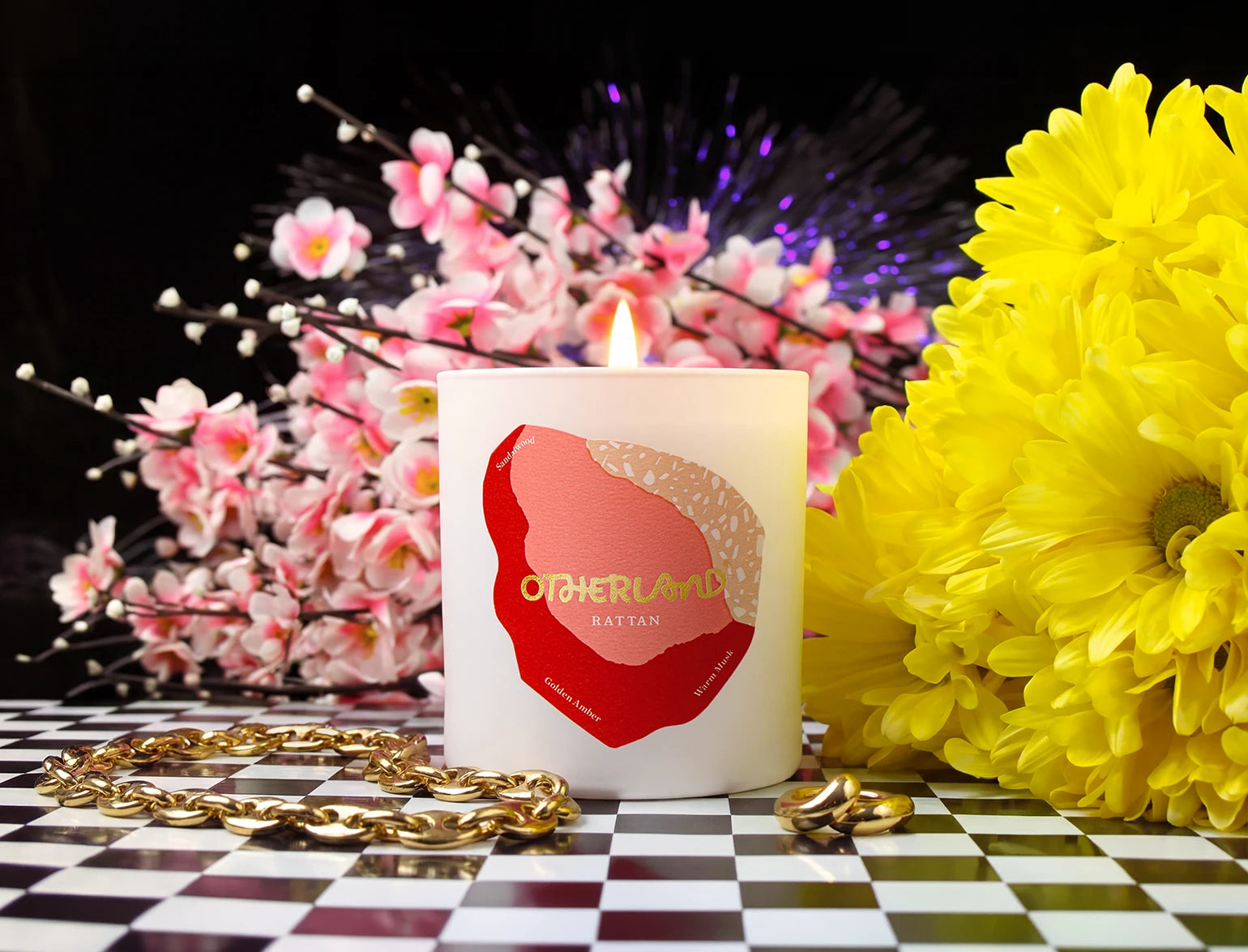 Candle with a red label on a checkered surface with flowers and jewelry