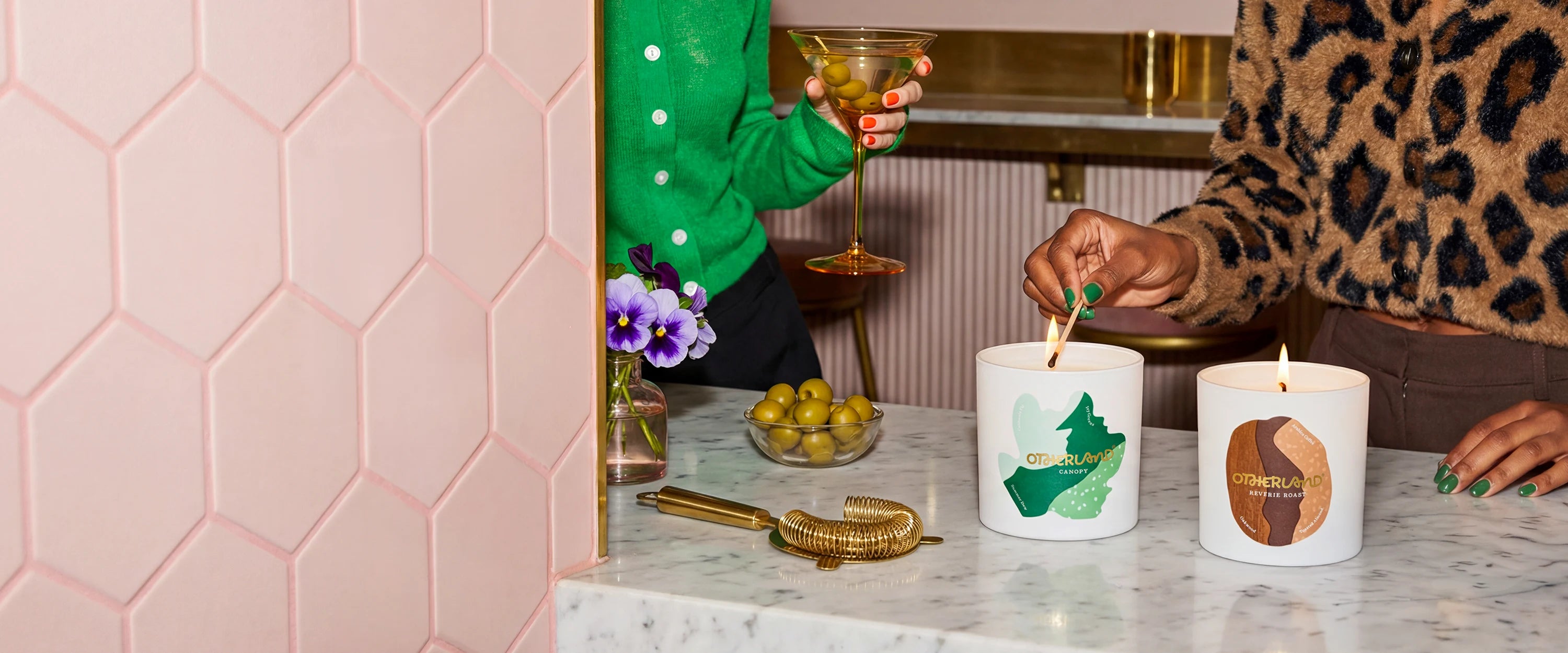 Two candles on a table with decorative items and people in the background.