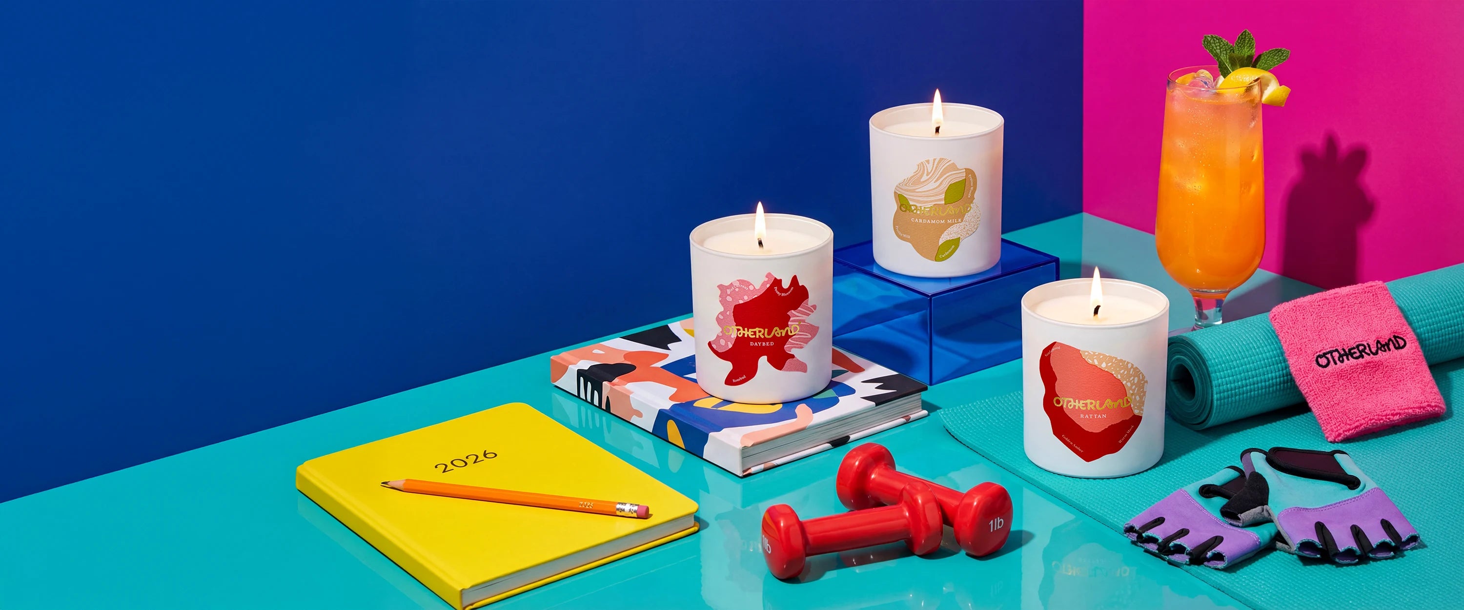 Colorful candles, notebook, pencil, and other items on a blue surface with a colorful background