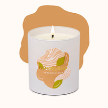 Candle in a white container with a label featuring an illustration of cardamom pods on a white background.