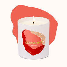 Rattan candle in a white container with a red and gold design, labeled 'Otherland' on a white background.