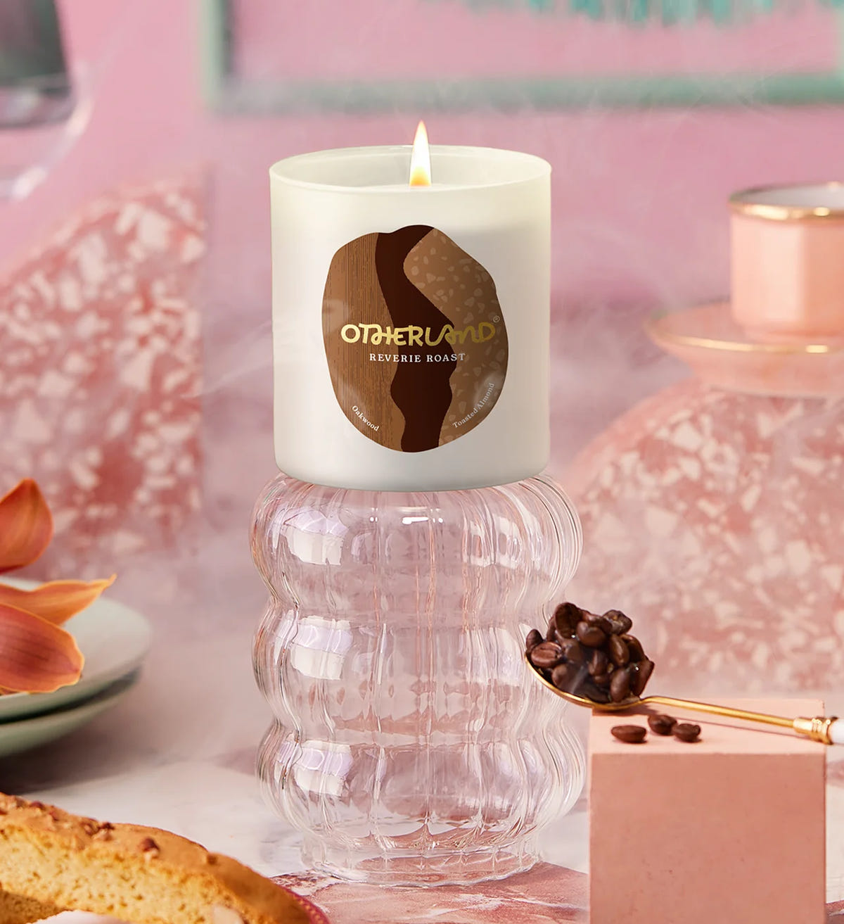 Candle with Otherland on a decorative surface with coffee beans and pastries.