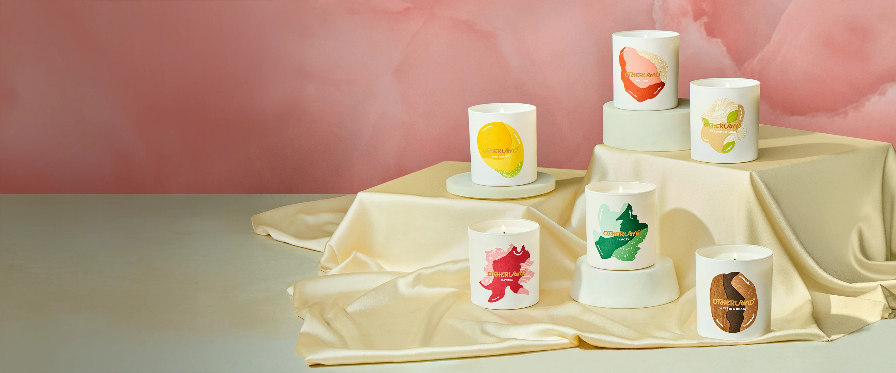 Set of candles with fruit designs on a beige cloth against a pink background