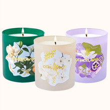 Three scented candles with floral designs on their containers against a white background.