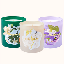 Three scented candles with floral designs on their containers against a white background.