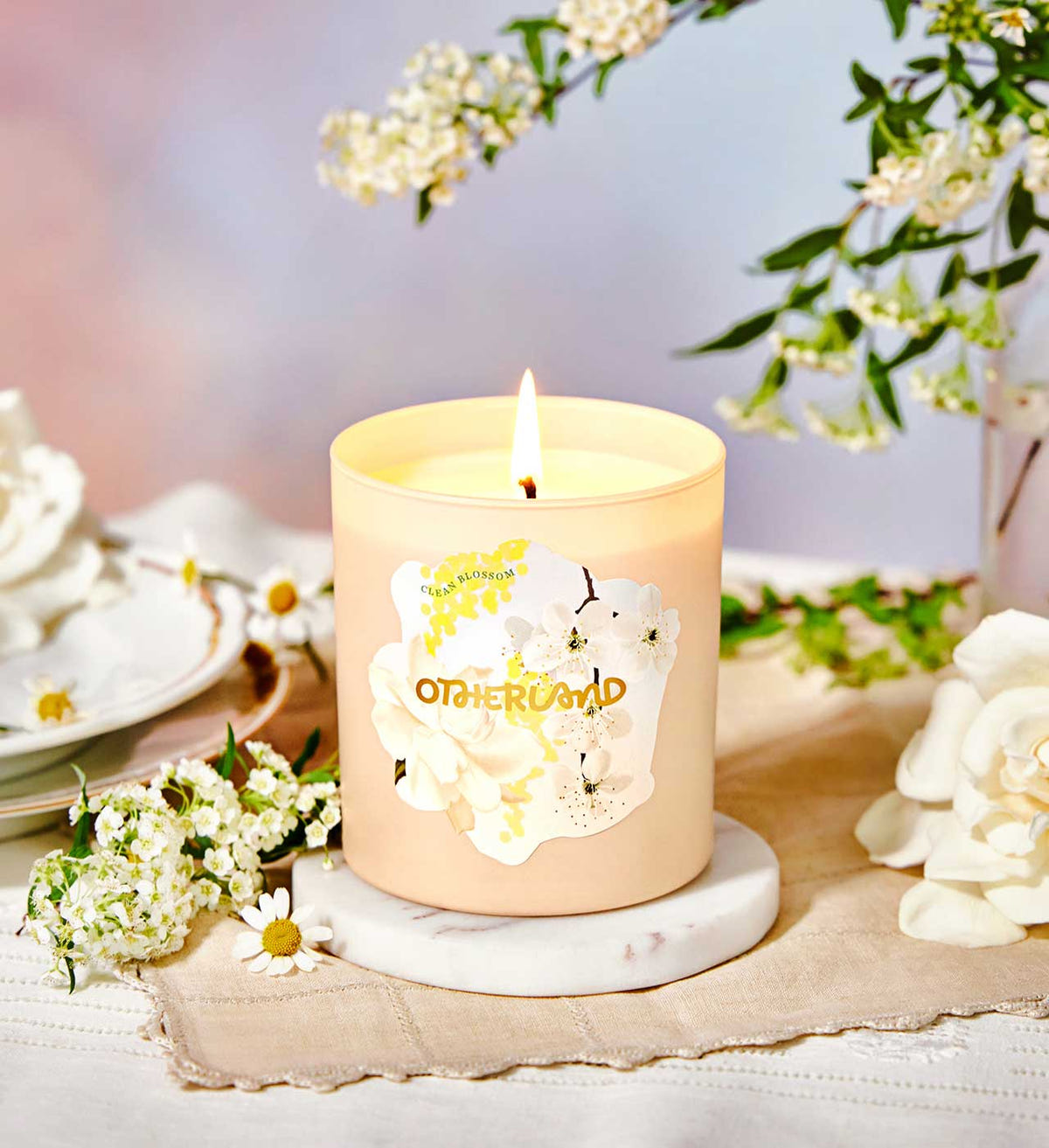 Candle with a floral design on a marble coaster surrounded by flowers and tea cups.
