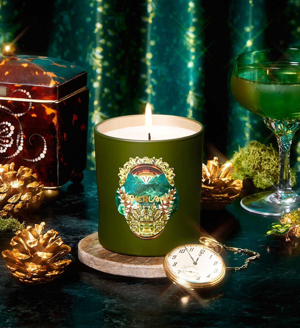 Green candle with a decorative label on a dark surface with decorative items.