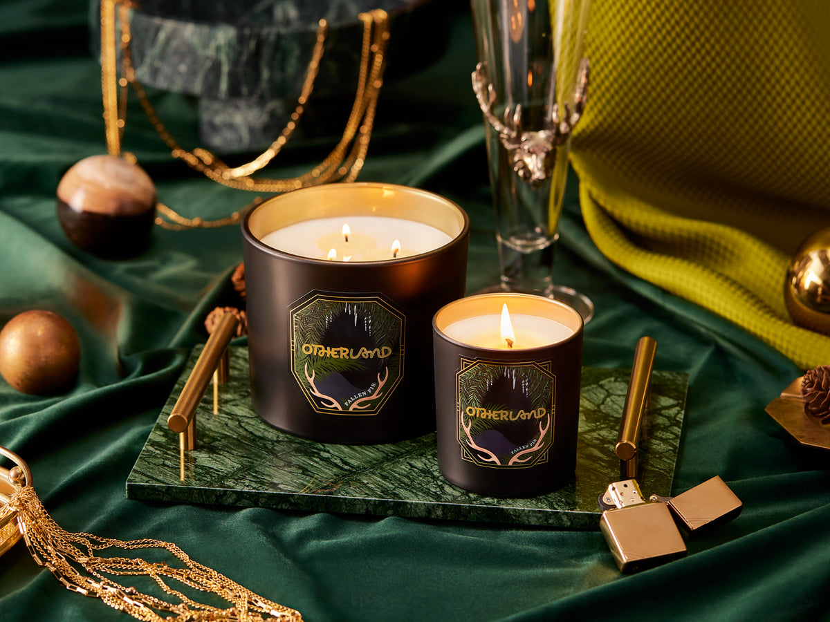 Two lit candles on a green surface with decorative items around them.