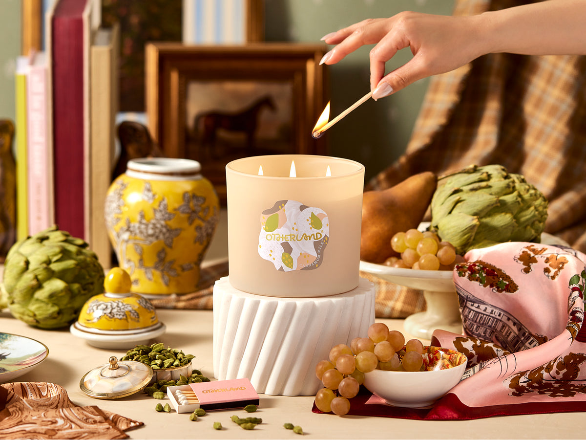 Candle being lit with a decorative setting of artichokes, grapes, and books.