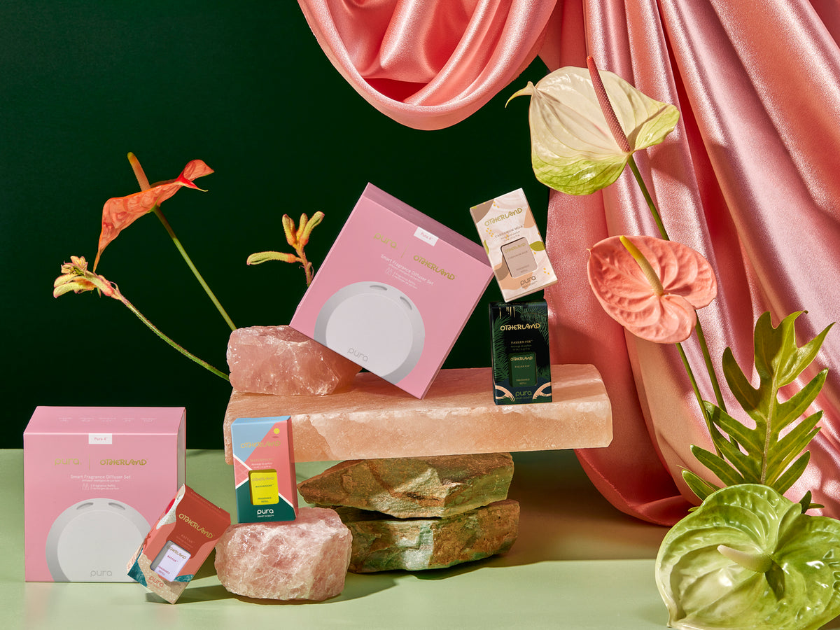 Pura diffuser and refills on a stone surface with pink drapes and plants in the background