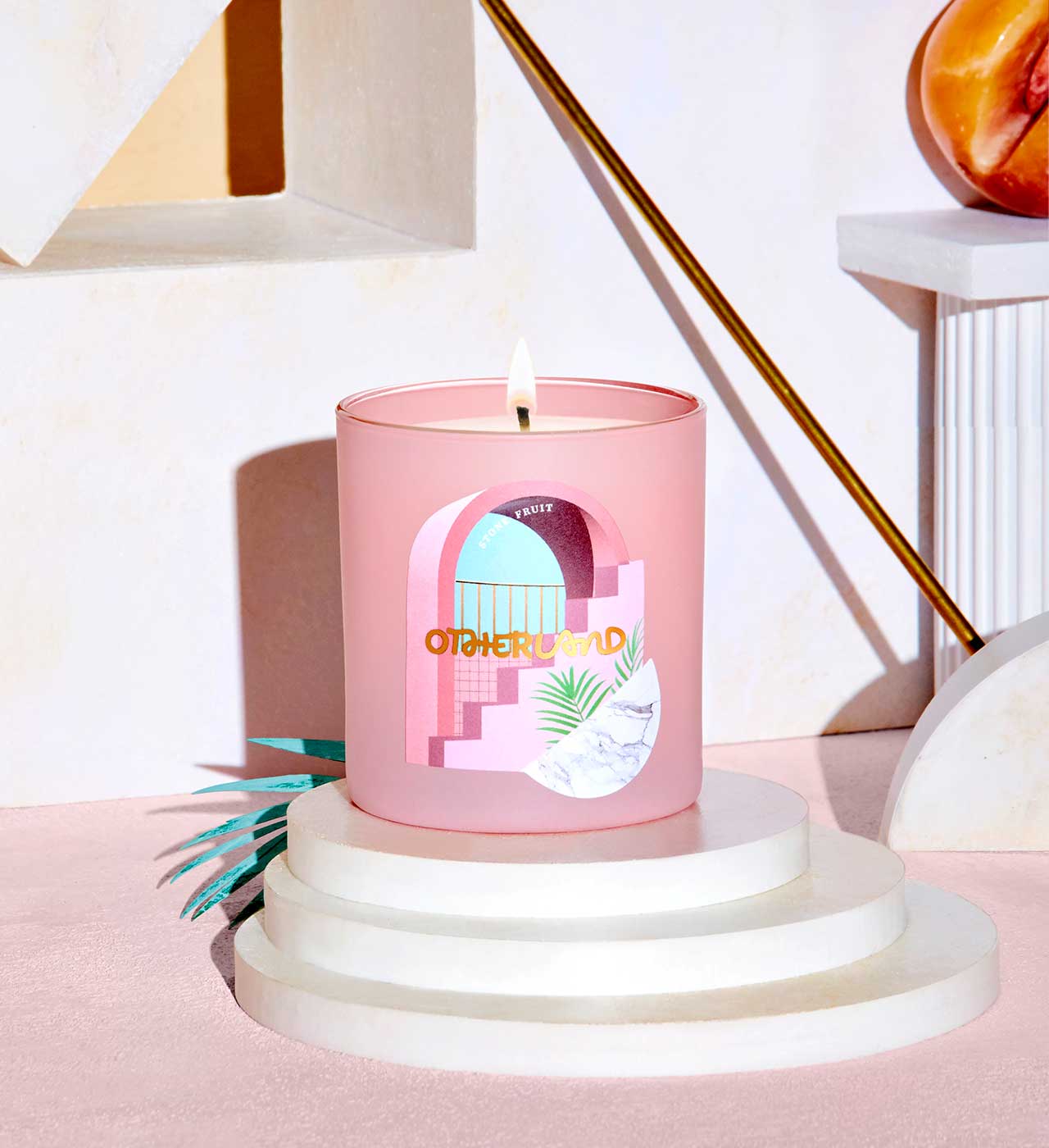 Pink candle with a decorative label on a white pedestal against a light pink background