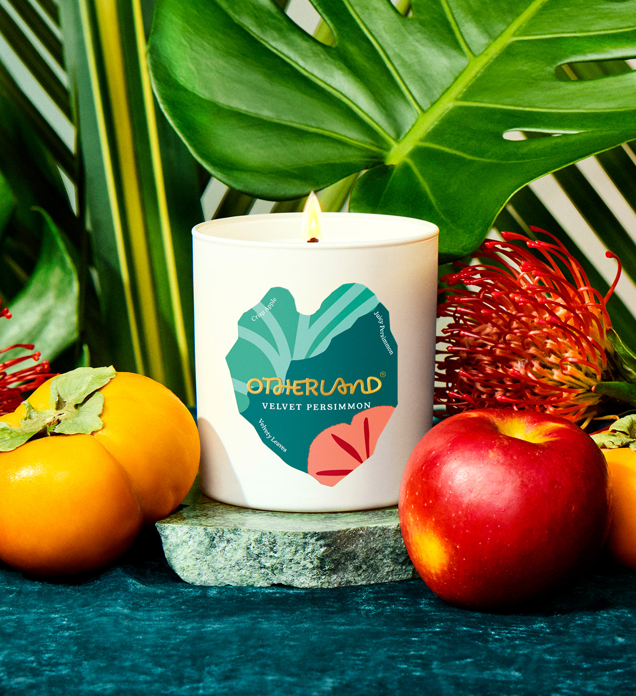 Candle with 'Otherland' branding surrounded by fruits and leaves - View 2